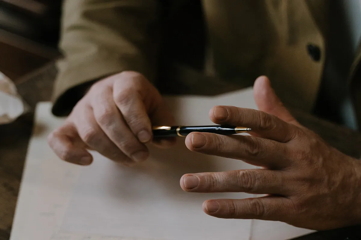 A writer's hands holding a fountain pen over a manuscript